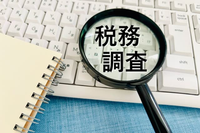 虫眼鏡の中に税務調査の文字があり、周りにはノートとキーボードが配置される